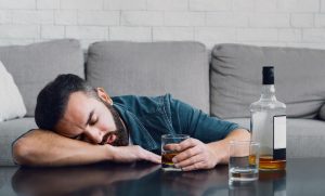 Alcohol addiction. Drunk man sleeping leaning on table with bottle and glass