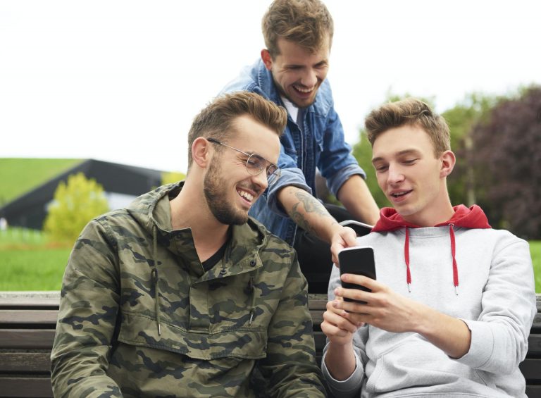 Happy men looking at smart phone and sitting on bench