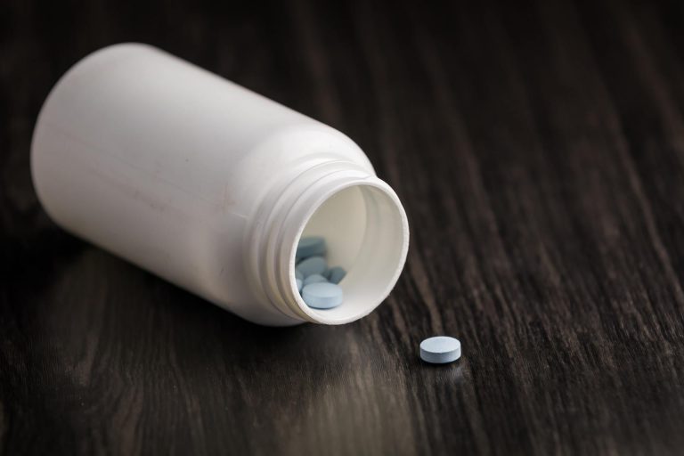 Medication pill in a row against a wood background. White pill bottle